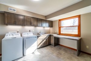 Custom laundry room with dark wood cabinetry, built-in sink, work surface, and washer/dryer in a Brookwood home in Fort Wayne, Indiana