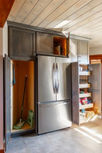 Custom kitchen cabinetry with built-in pantry, pull-out shelves, and broom closet surrounding a stainless steel refrigerator in a Brookwood home in Fort Wayne, Indiana