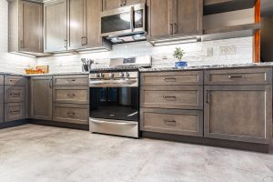 Custom modern kitchen with gray wood cabinetry, built-in microwave, stainless steel appliances, and granite countertops in a Brookwood home in Fort Wayne, Indiana