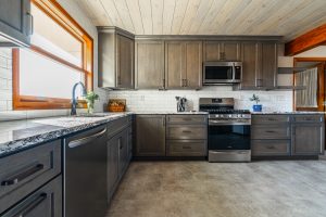 Custom modern kitchen with brown wood cabinetry, stainless steel appliances, granite countertops, and built-in microwave in a Brookwood home in Fort Wayne, Indiana