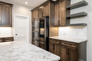 Custom modern kitchen with warm wood cabinetry, granite countertops, stainless steel appliances, and floating shelves in a Brookwood home in Fort Wayne, Indiana